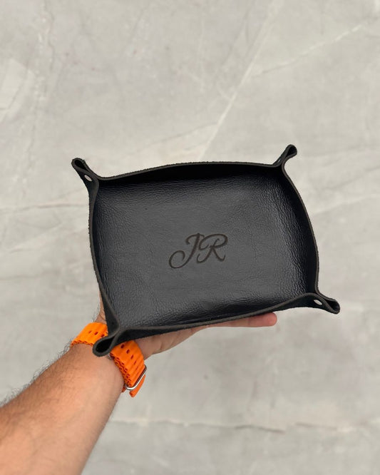 Caja multifuncional de cuero negro en la mano, con unas iniciales grabadas en el fondo