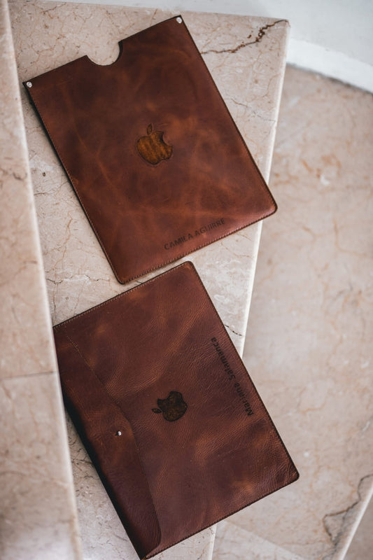 Estuche de cuero miel para iPad con un logo y un nombre grabados; abajo, un estuche de portátil