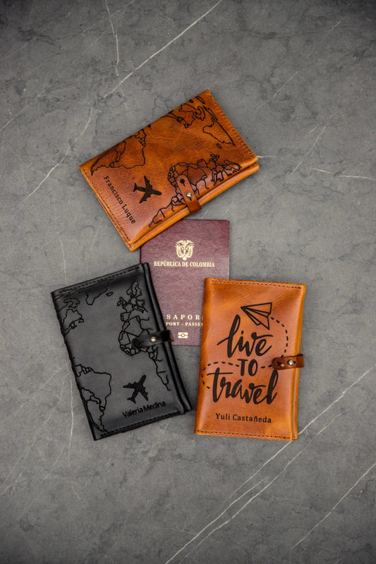 Tres portapasaportes dobles cerrados, en cuero rústico miel y negro, con los diseños Mapa y Live to Travel, junto a un pasaporte