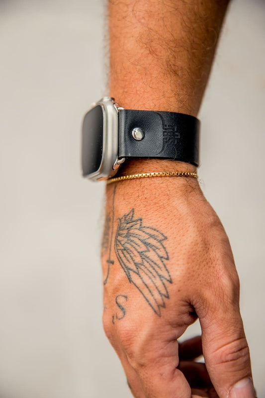 Pulso de cuero negro para Apple Watch en la muñeca, con unas iniciales grabadas y un remache metálico