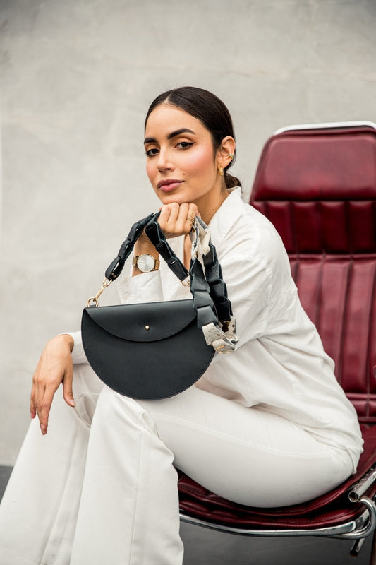 Mujer con un bolso media luna de cuero negro, con la tapa y su broche, y correa trenzada de cuero y pelaje