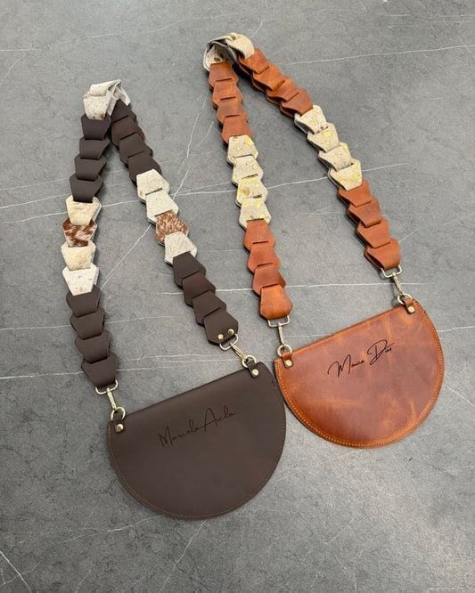 Dos bolsos media luna de cuero café y rústico miel vistos por detrás, con un nombre grabado en cada uno