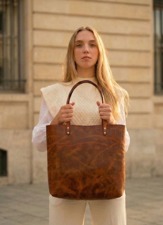 Mujer sosteniendo de frente un bolso tote de cuero rústico miel con asas delgadas