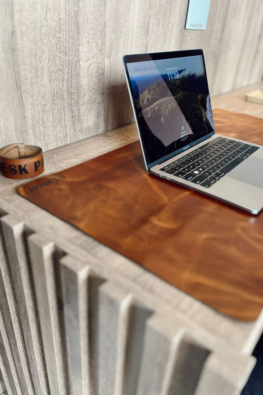Desk pad de cuero miel en un escritorio, con un portátil encima y una tira de cuero al lado