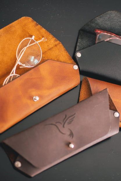 Estuches para gafas en cuero café y rústico miel; el café con un colibrí grabado y el miel abierto con unas gafas