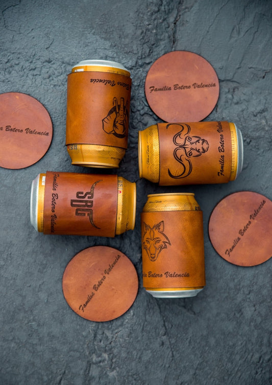 Cuatro forros de cuero rústico miel para latas con grabados distintos, vistos desde arriba, entre portavasos
