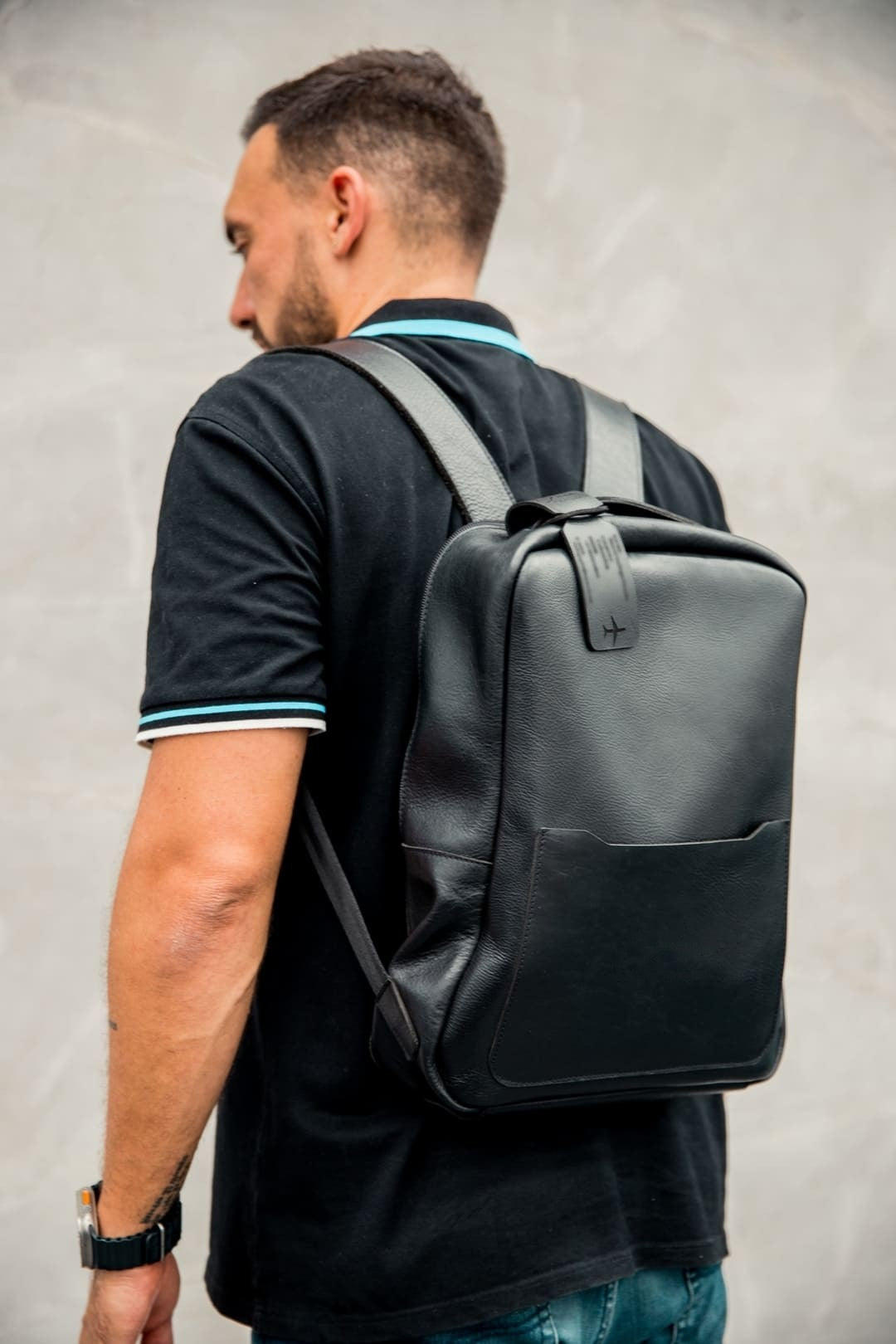 Hombre con un maletín tipo morral de cuero negro puesto en la espalda