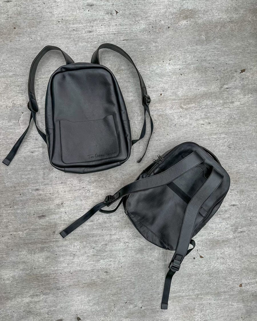 Dos maletines tipo morral de cuero negro: uno de frente con un nombre grabado en el bolsillo y otro por detrás, con sus correas