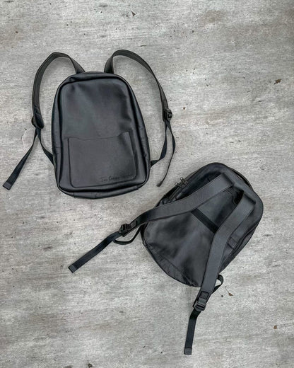 Dos maletines tipo morral de cuero negro: uno de frente con un nombre grabado en el bolsillo y otro por detrás, con sus correas