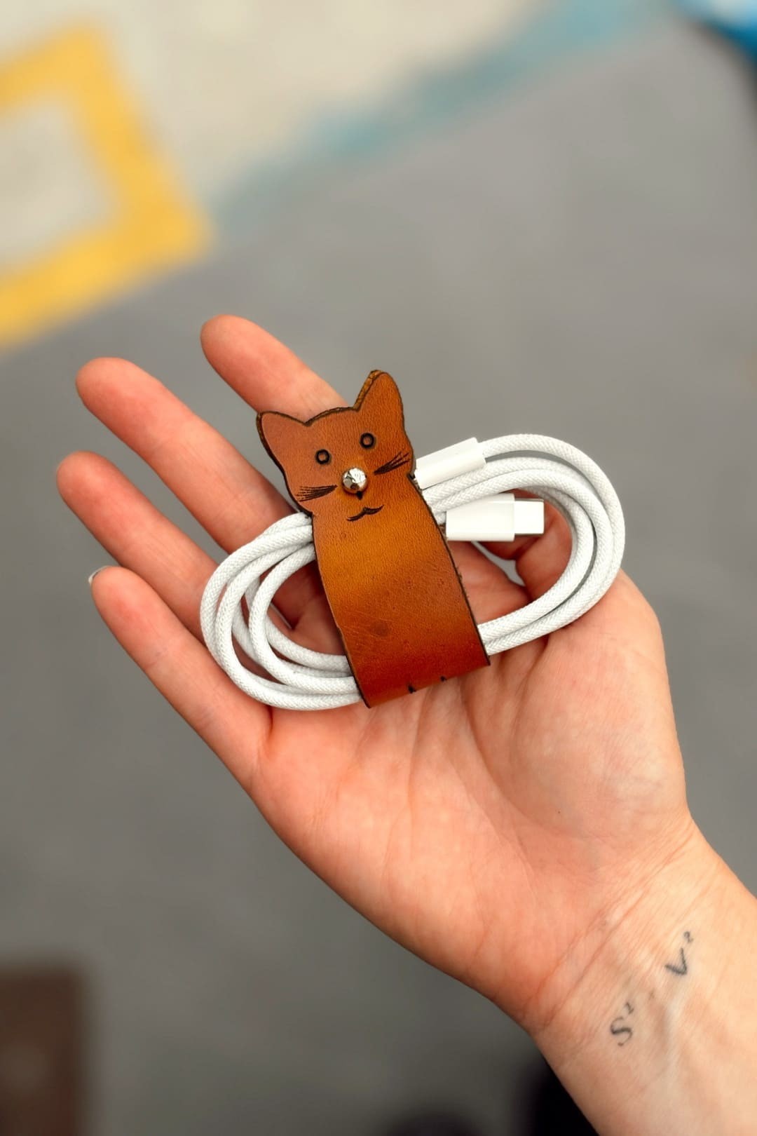 Organizador de cable en cuero miel con forma de gato, con un cable enrollado, en la palma de la mano