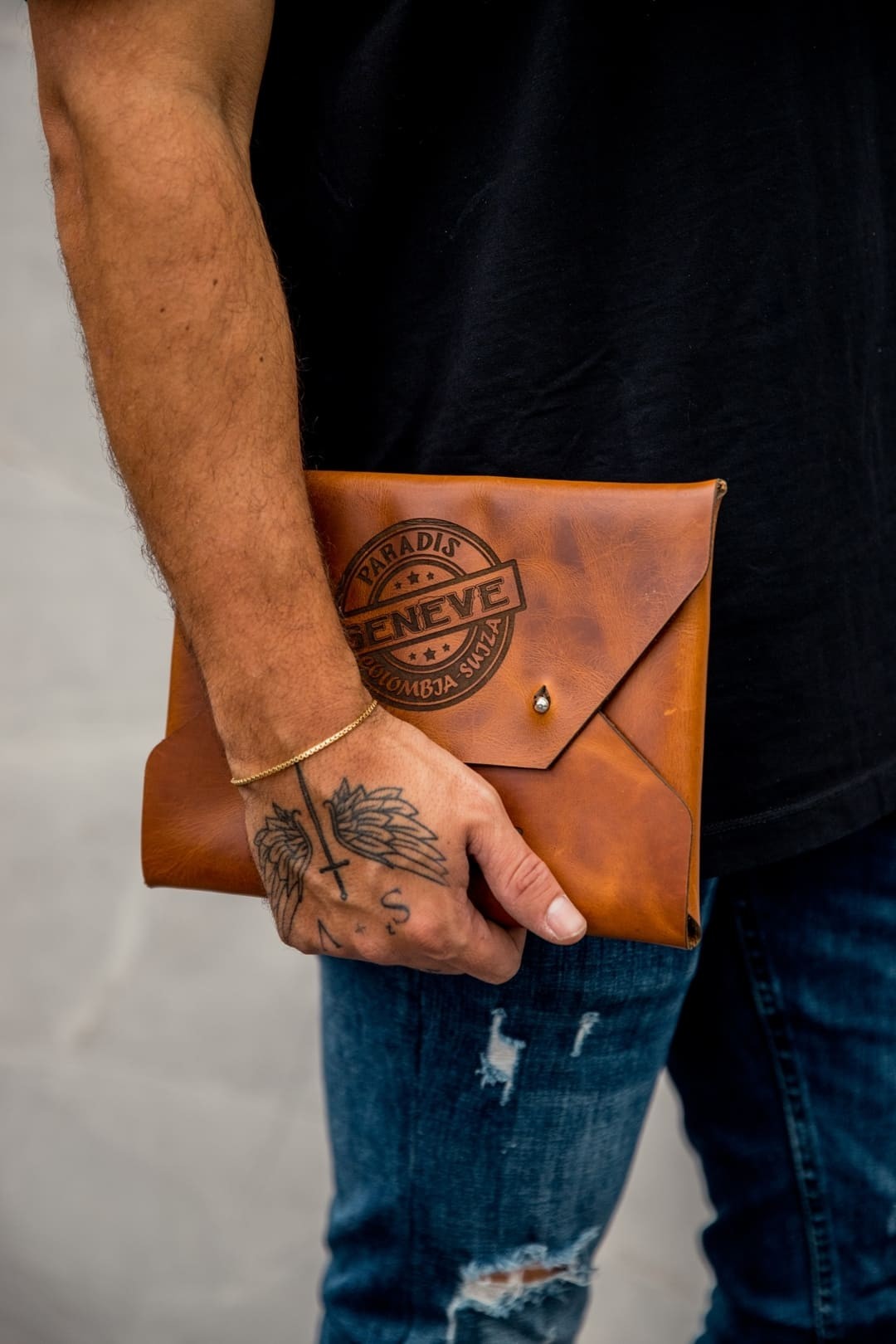Hombre llevando en la mano el sobre grande de cuero rústico miel, con un logo grabado en la solapa